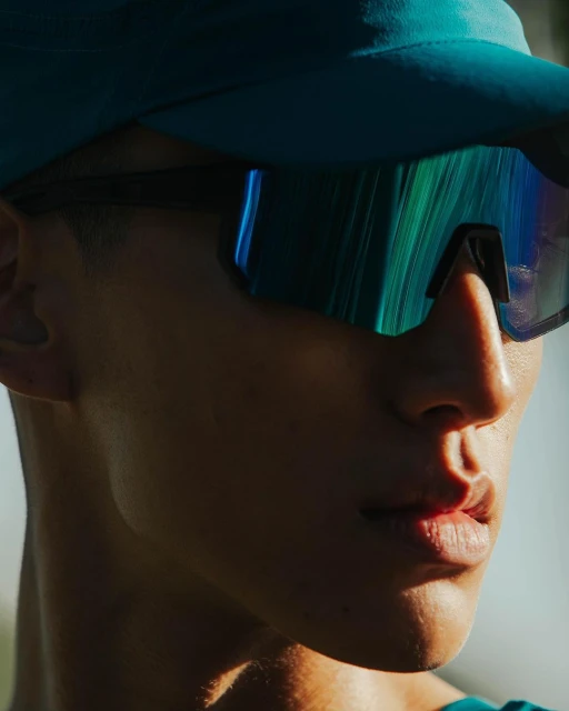Close-up of an adult with turquoise cap and sunglasses reflecting green and blue, showcasing a modern and sporty aesthetic.