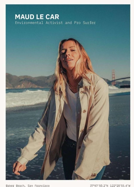 Woman with long hair standing on a beach near the ocean with a bridge in the background wearing a jacket on a sunny day.
