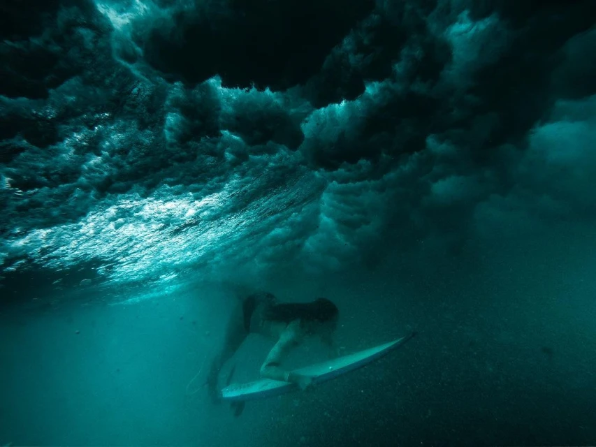 Underwater shot of a surfer riding a wave on a surfboard, turquoise water. Ocean photography with wave texture details and underwater view.