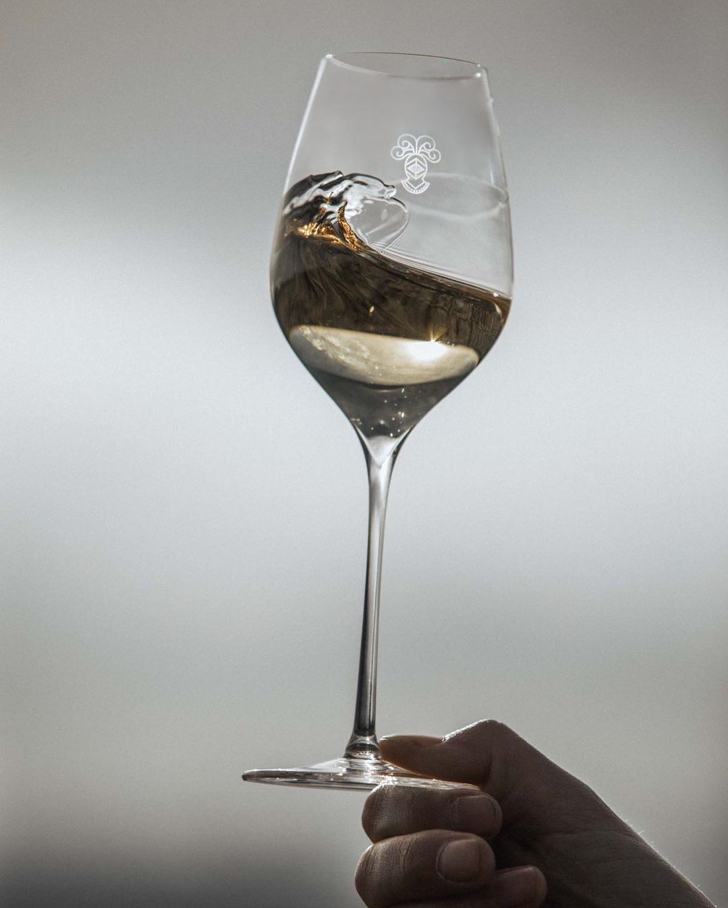Wine glass held by a hand with light reflecting off liquid inside against grey background, ideal for beverage product promotion.