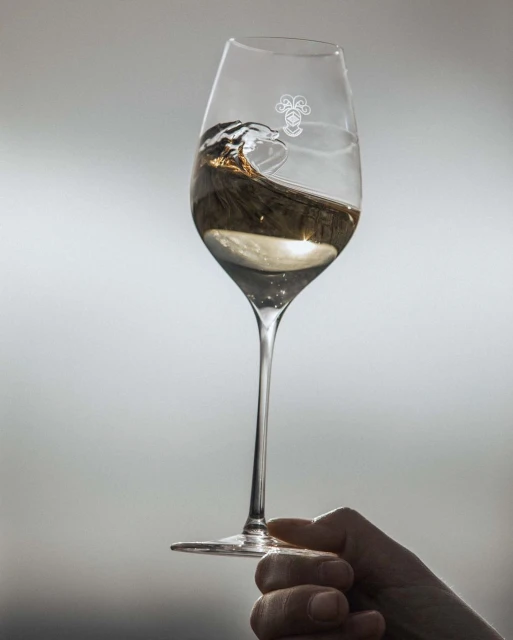 Wine glass held by a hand with light reflecting off liquid inside against grey background, ideal for beverage product promotion.