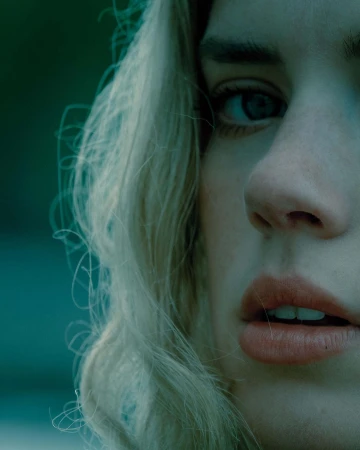 Close-up portrait of a blonde woman with blue eyes and parted lips, photographed in moody tones by Sebastien Zanella.