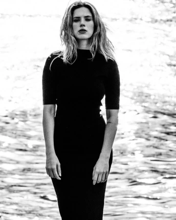 Black and white portrait of a woman in a black midi dress standing outdoors near shimmering water.