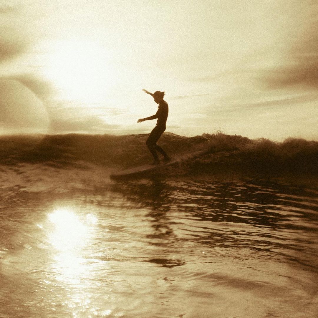 A lone surfer rides a wave at sunset in a monochrome image, capturing the essence of a solo water sport activity.