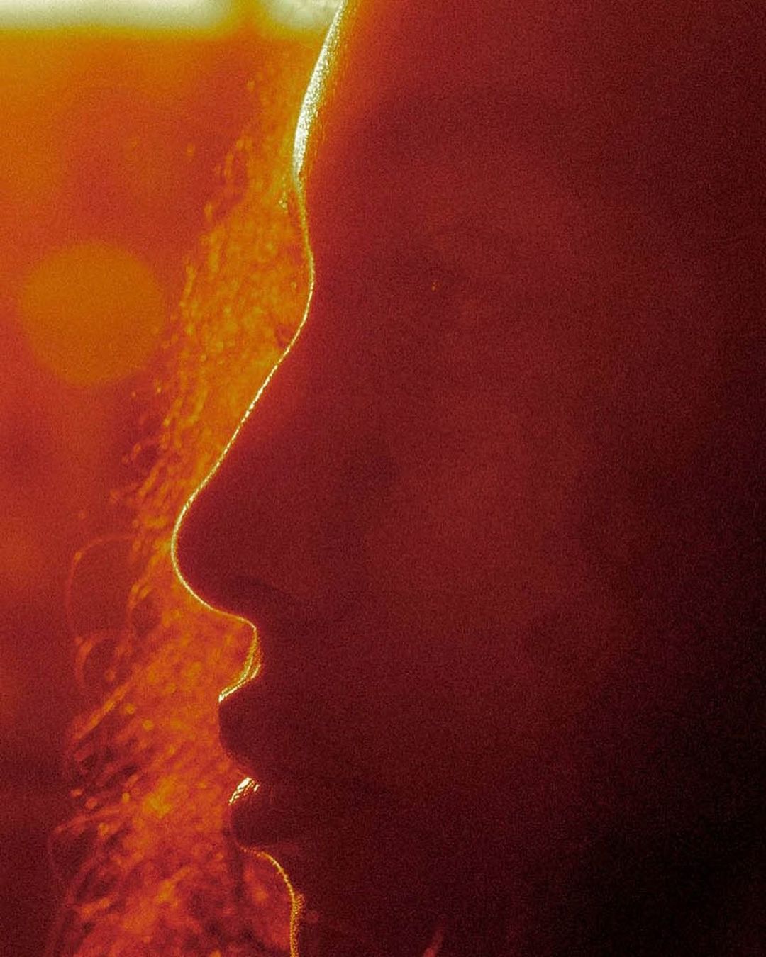 Close-up profile of a person with curly hair, silhouetted against a bright orange background, creating a warm and vibrant visual.