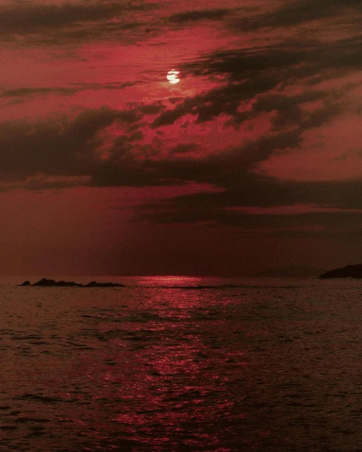 Monochromatic red scenic of the sun setting over the ocean with dark storm clouds and calm water reflecting the light in the evening.