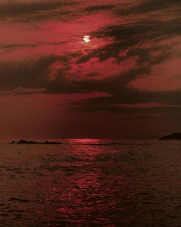 Monochromatic red scenic of the sun setting over the ocean with dark storm clouds and calm water reflecting the light in the evening.