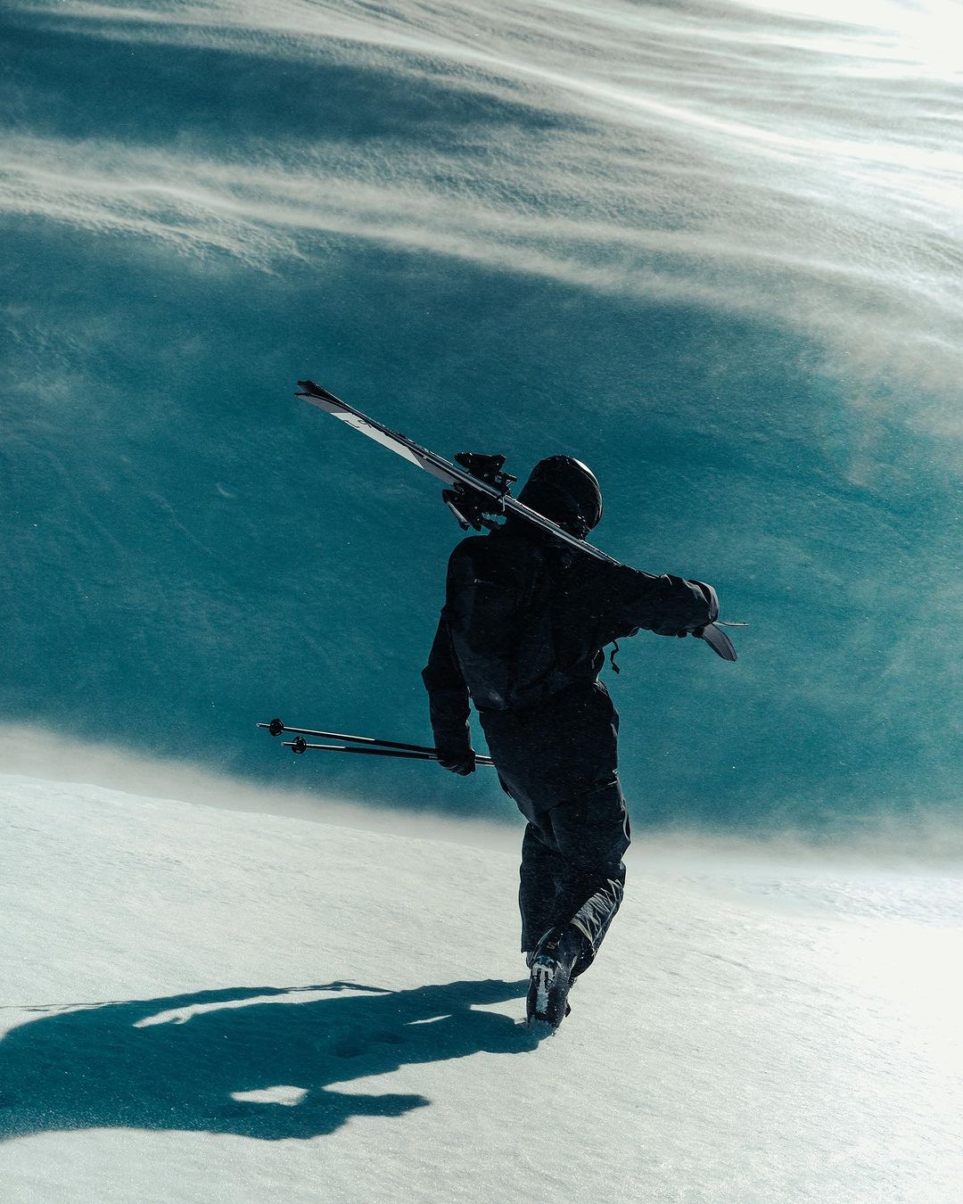 A person in ski gear walks through a snowy mountain landscape with skis and poles, showcasing winter sports and outdoor activities.