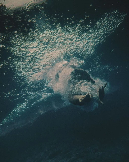 Underwater shot of a person swimming in deep, blue water with sunlight filtering through the surface, creating bubbles and a sense of depth.