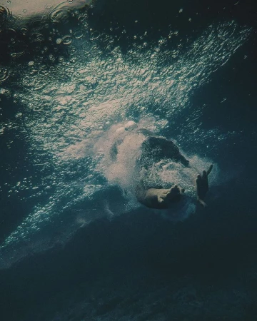 Underwater shot of a person swimming in deep, blue water with sunlight filtering through the surface, creating bubbles and a sense of depth.