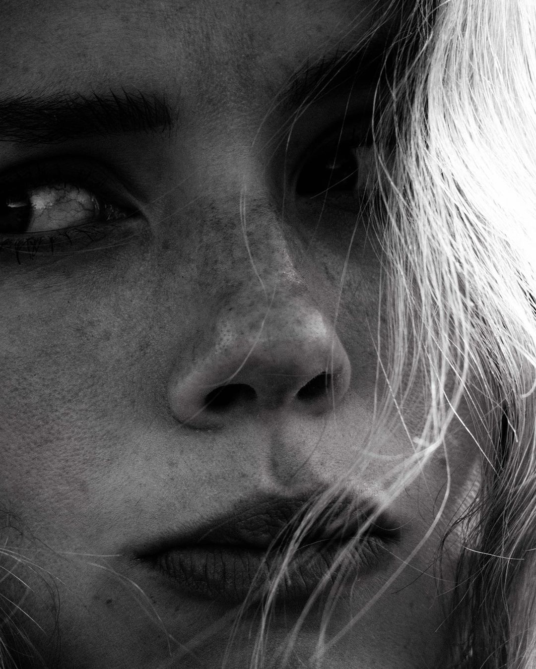 Monochrome portrait of a woman with light hair, focusing on her face with visible freckles, soft lighting, and shallow depth of field.