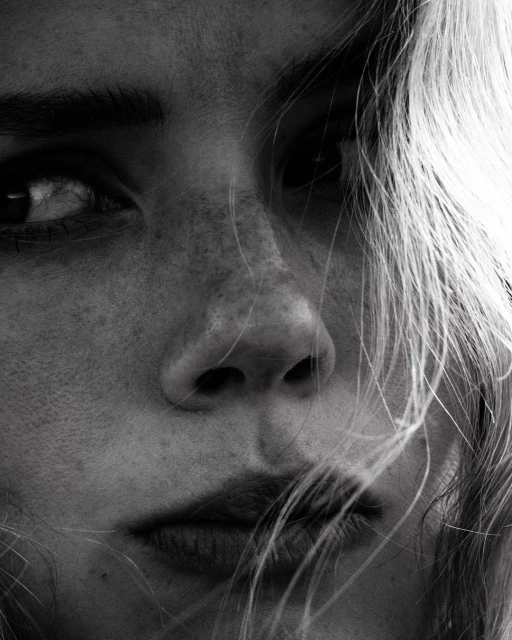 Monochrome portrait of a woman with light hair, focusing on her face with visible freckles, soft lighting, and shallow depth of field.