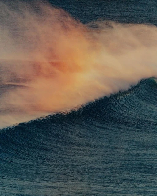 A powerful ocean wave curls toward the camera, its form blurred with motion, beneath a sky streaked with orange and purple hues.