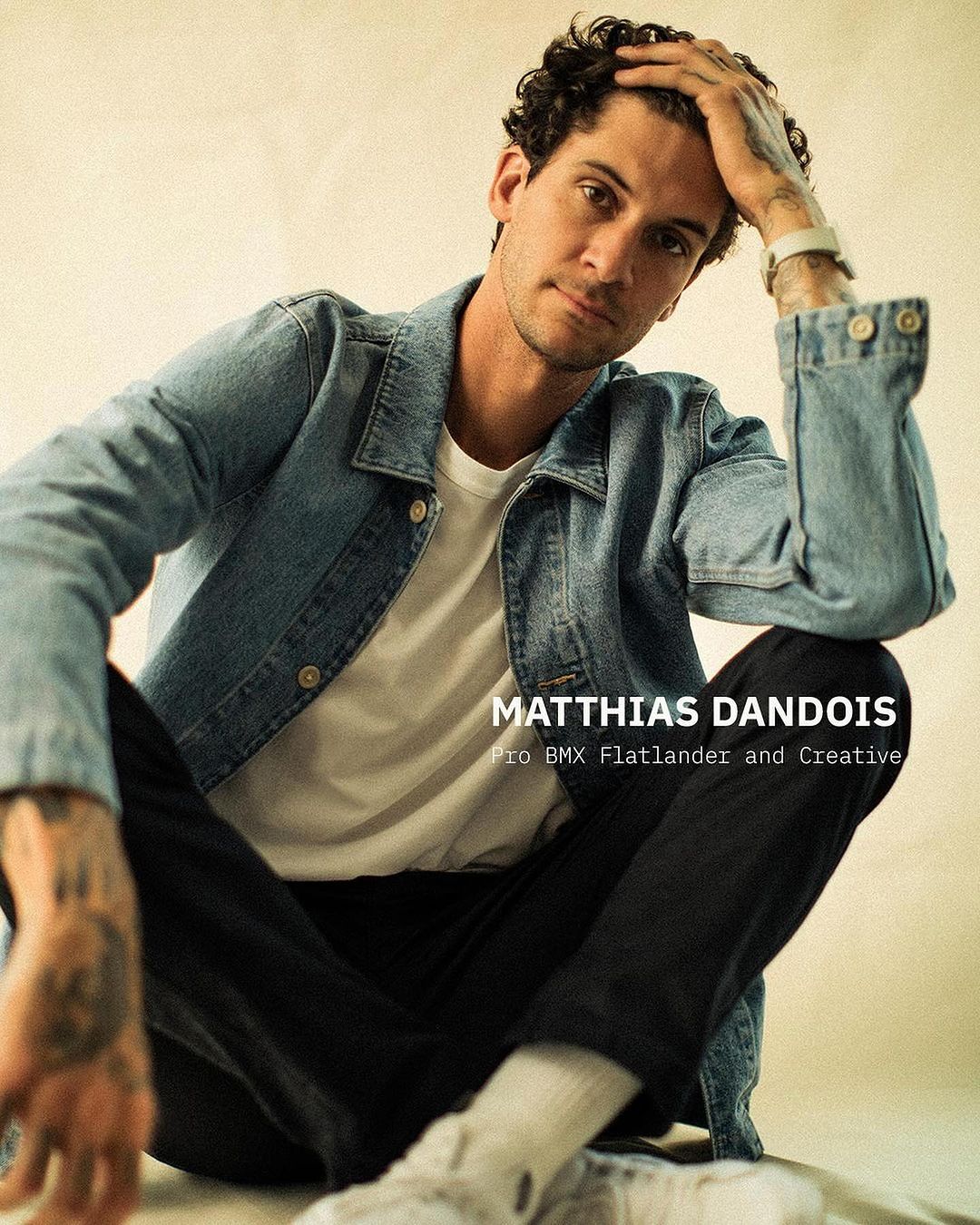 Portrait of Matthias Dandois, a pro BMX flatlander, in a denim jacket and dark pants, casually seated against a neutral background.