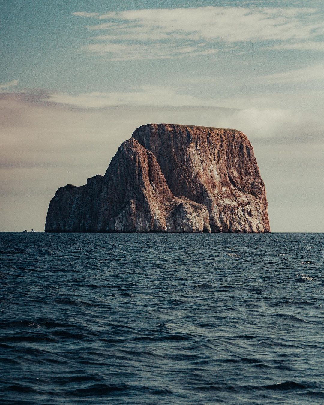 Scenic view of a large, rocky island in the middle of the ocean under a partly cloudy sky on a clear day, landscape photograph.