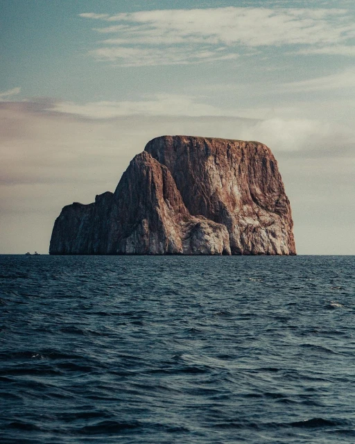 Scenic view of a large, rocky island in the middle of the ocean under a partly cloudy sky on a clear day, landscape photograph.