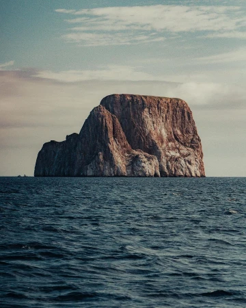 Scenic view of a large, rocky island in the middle of the ocean under a partly cloudy sky on a clear day, landscape photograph.