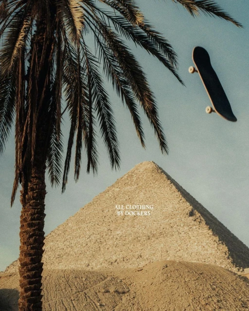 Low-angle shot of skateboard in mid-air near a palm tree and pyramid under a blue sky, showcasing urban and travel themes.
