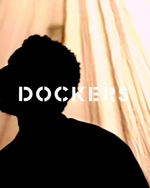 Portrait of silhouetted figure with white Dockers logo in the foreground, on tan, draped fabric. Fashion advertisement.