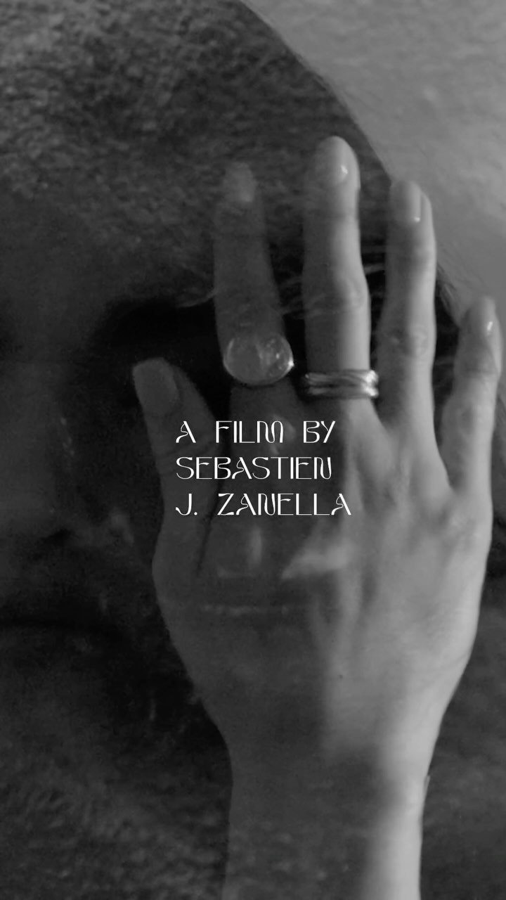 Close-up shot in monochrome of an adult female's hand with rings, film title text overlay, creating an atmospheric and moody visual narrative.