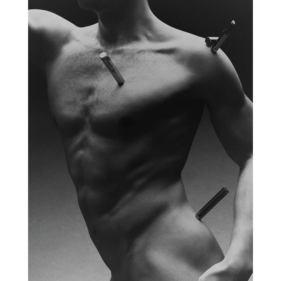 Artistic black and white portrait of a shirtless adult male with bars piercing his skin in a minimalist studio setting with soft lighting.