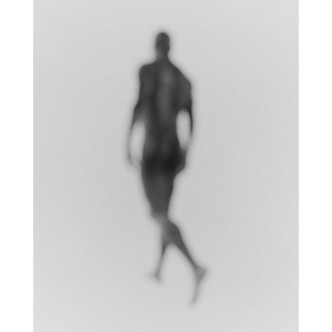 Monochromatic image of a male figure walking against a bright, soft-focus backdrop, creating a minimalist, artistic effect.