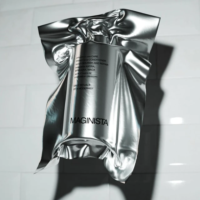 Product shot of a silver foil-wrapped bottle of Maginista hair care product against a white tiled wall with soft, diffused lighting.