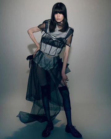 Model wearing sheer black layered dress and thigh-high stockings against a neutral studio background.
