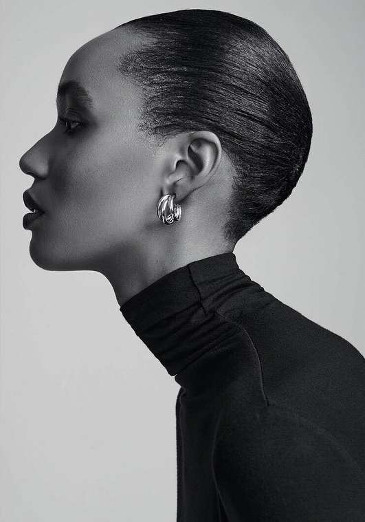 Close-up profile of a woman with an elegant black turtleneck and silver hoop earrings against a soft grey background, showcasing beauty and style.