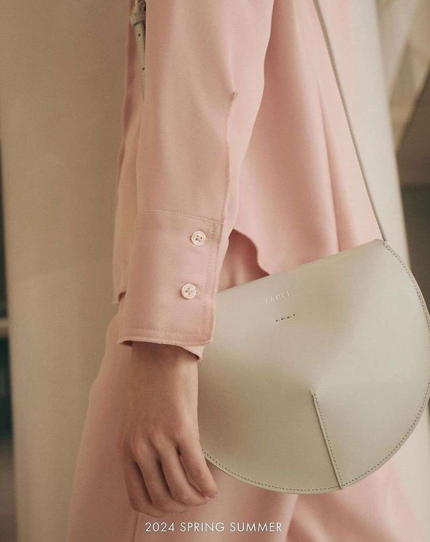 Fashion shot featuring a woman with a stylish white half-moon bag, wearing a light pink outfit, and standing against a blurred background.