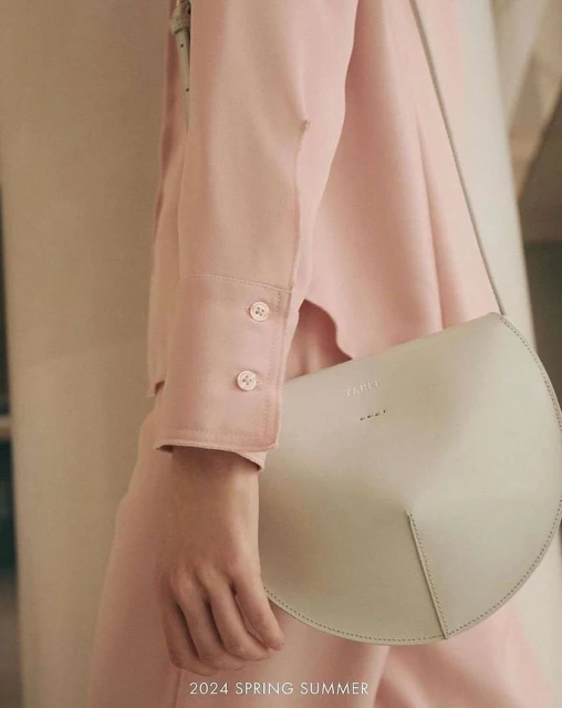 Fashion shot featuring a woman with a stylish white half-moon bag, wearing a light pink outfit, and standing against a blurred background.