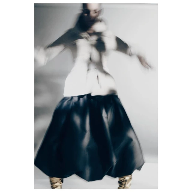 Abstract fashion shot featuring a person in a white top and black skirt with golden boots, soft focus and motion blur, against a light backdrop.