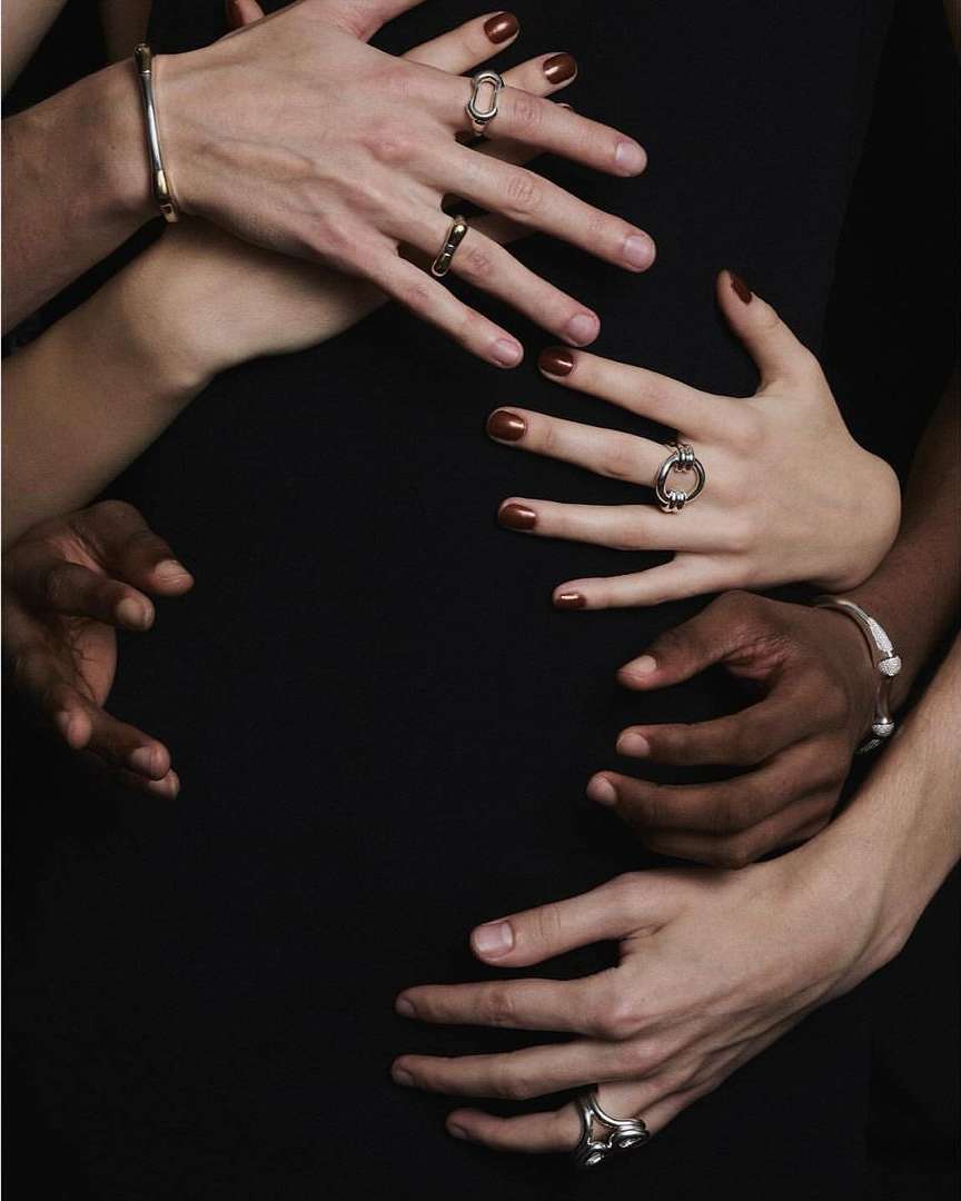 Close-up studio shot of six human hands adorned with rings and bracelets, creating an intriguing composition against a dark background.