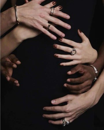 Close-up studio shot of six human hands adorned with rings and bracelets, creating an intriguing composition against a dark background.