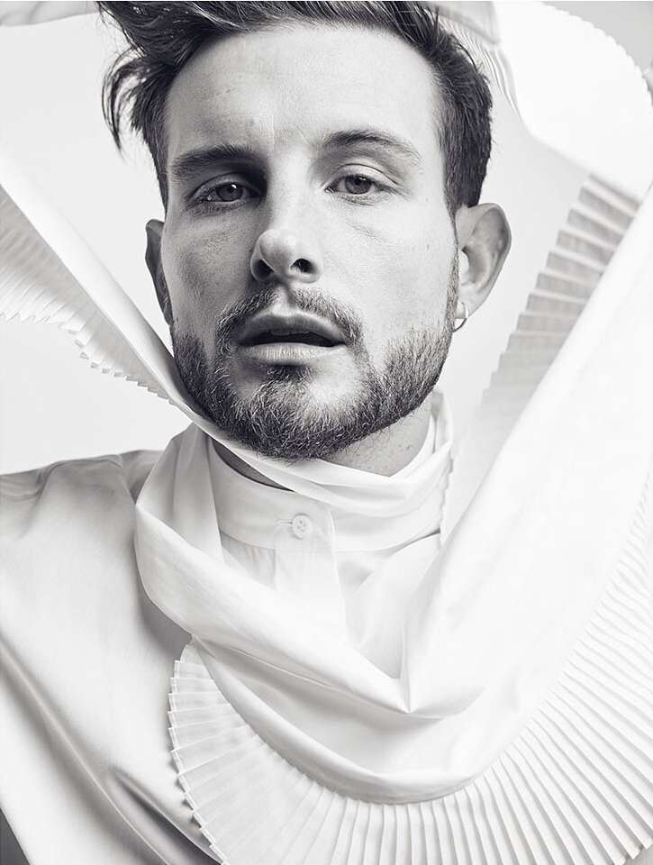 Black and white portrait of a man with a beard wearing a white shirt with a pleated ruff against a stark white background.