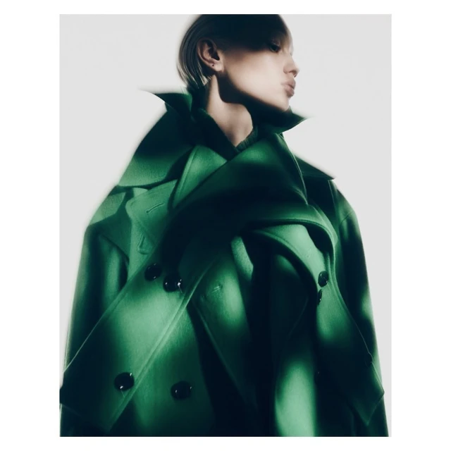 Fashion editorial shot of an adult female model in a vibrant green coat against a clean white backdrop, showcasing modern style.