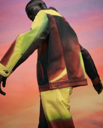 Black man wearing a gradient yellow and red jacket and matching trousers against a sunset sky background photographed by Seiji Fujimori.