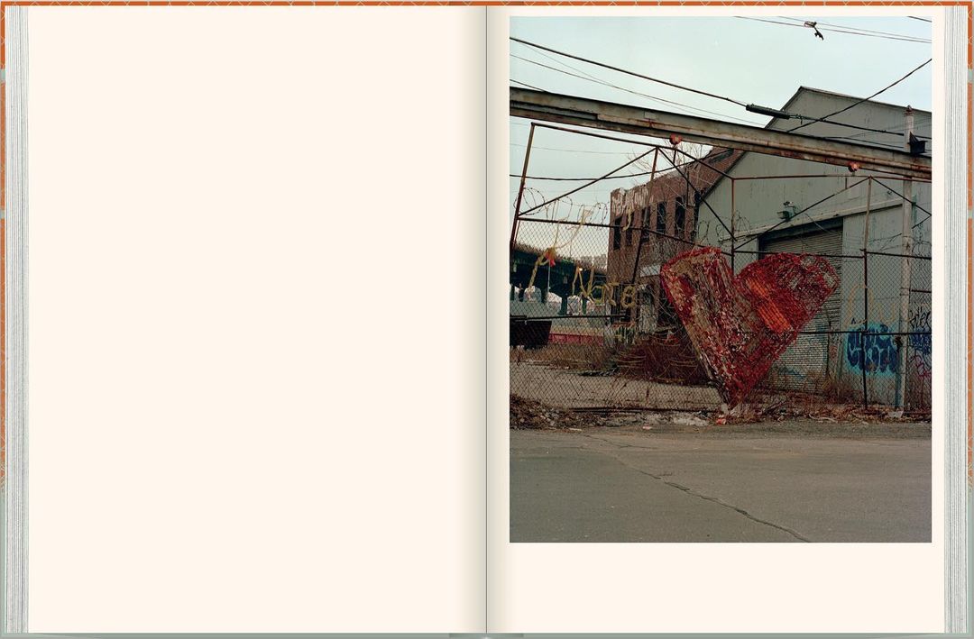 Open book features a photograph of an outdoor urban scene with a heart-shaped wire sculpture on a chain-link fence near buildings.