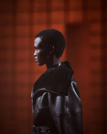 Profile portrait of a model with short hair wearing a dark leather coat against a warm red-toned background