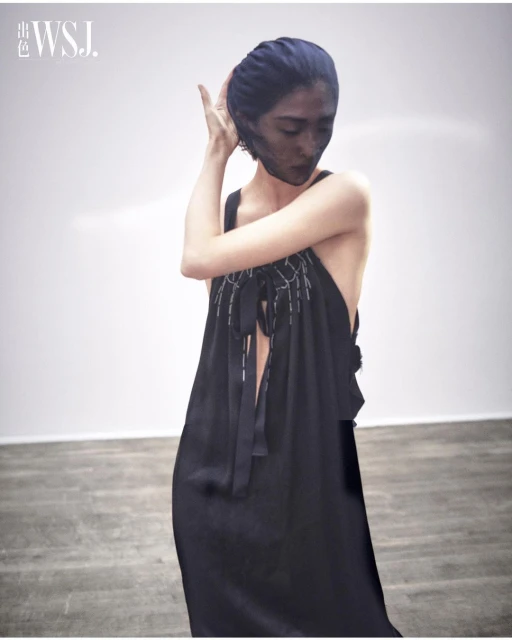 Elegant fashion shot of a woman in a black sleeveless dress and black sheer face covering against a white background in a studio.