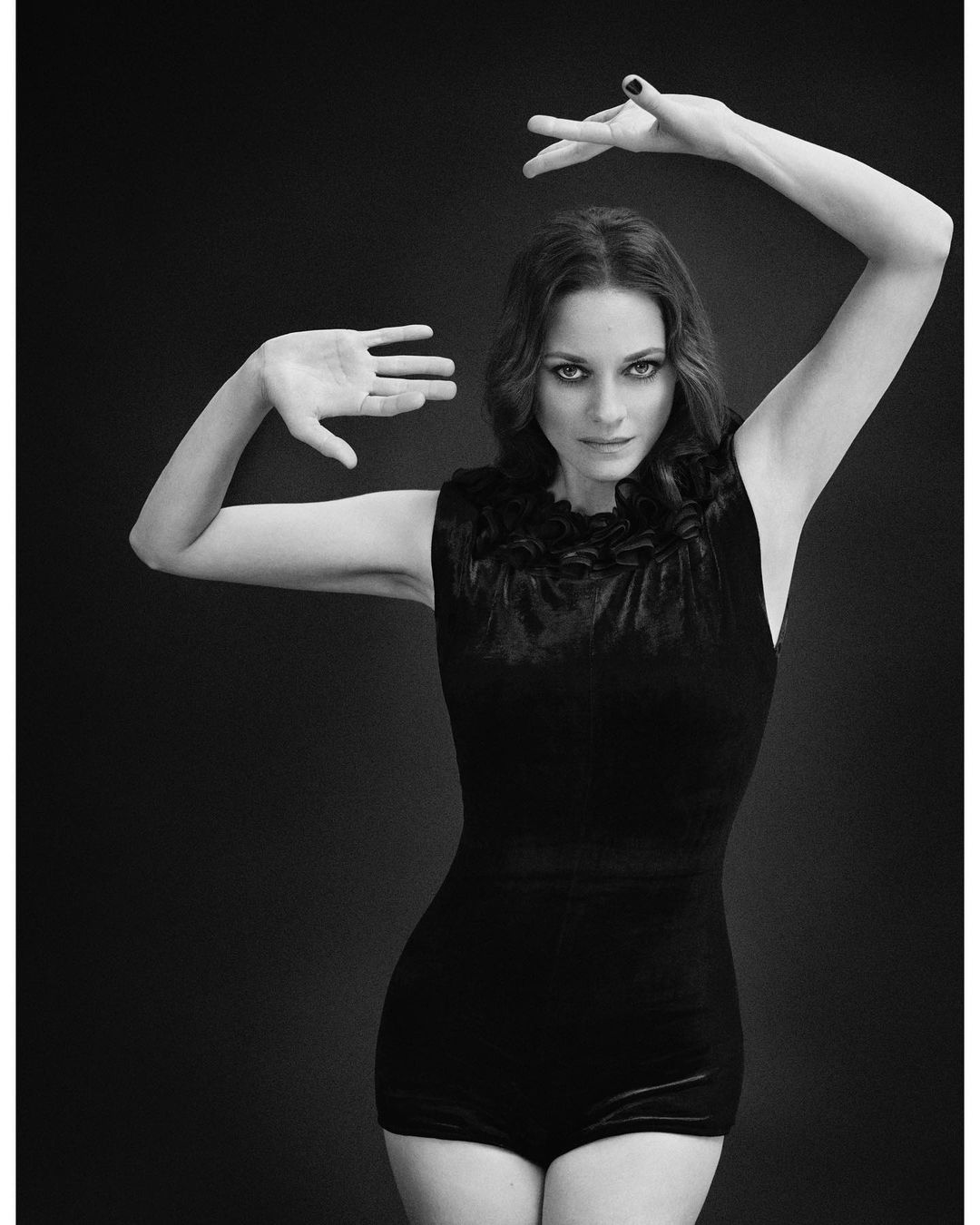 Monochrome portrait of Marion Cotillard wearing a sleeveless dark leotard, posing with hands raised.