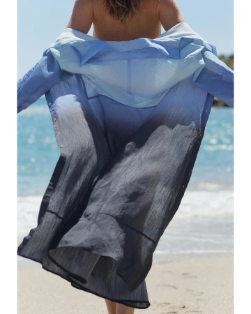 Model from behind wearing an ombré blue linen shirt on a sandy beach by the ocean