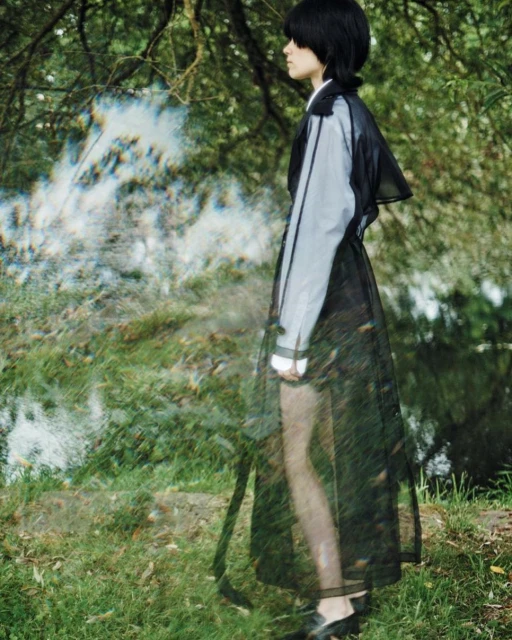 A person in a translucent dress poses in a grassy outdoor setting with blurred motion effect and dappled lighting.