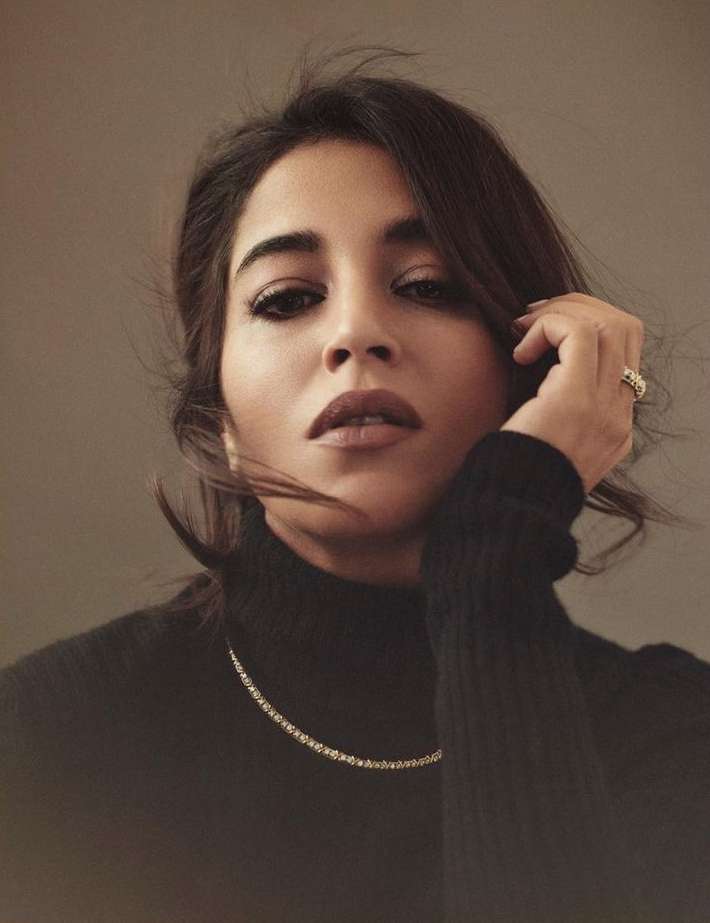 Close-up portrait of a woman in a black turtleneck sweater wearing a delicate gold necklace and ring, shot by Serge Leblon.