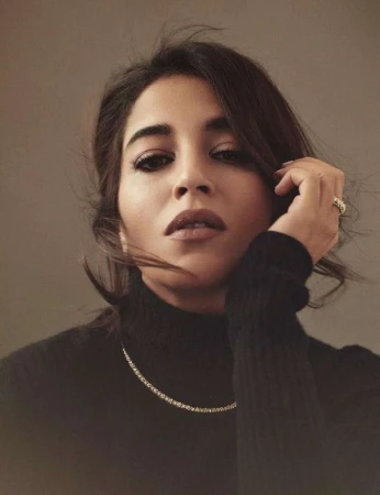 Close-up portrait of a woman in a black turtleneck sweater wearing a delicate gold necklace and ring, shot by Serge Leblon.