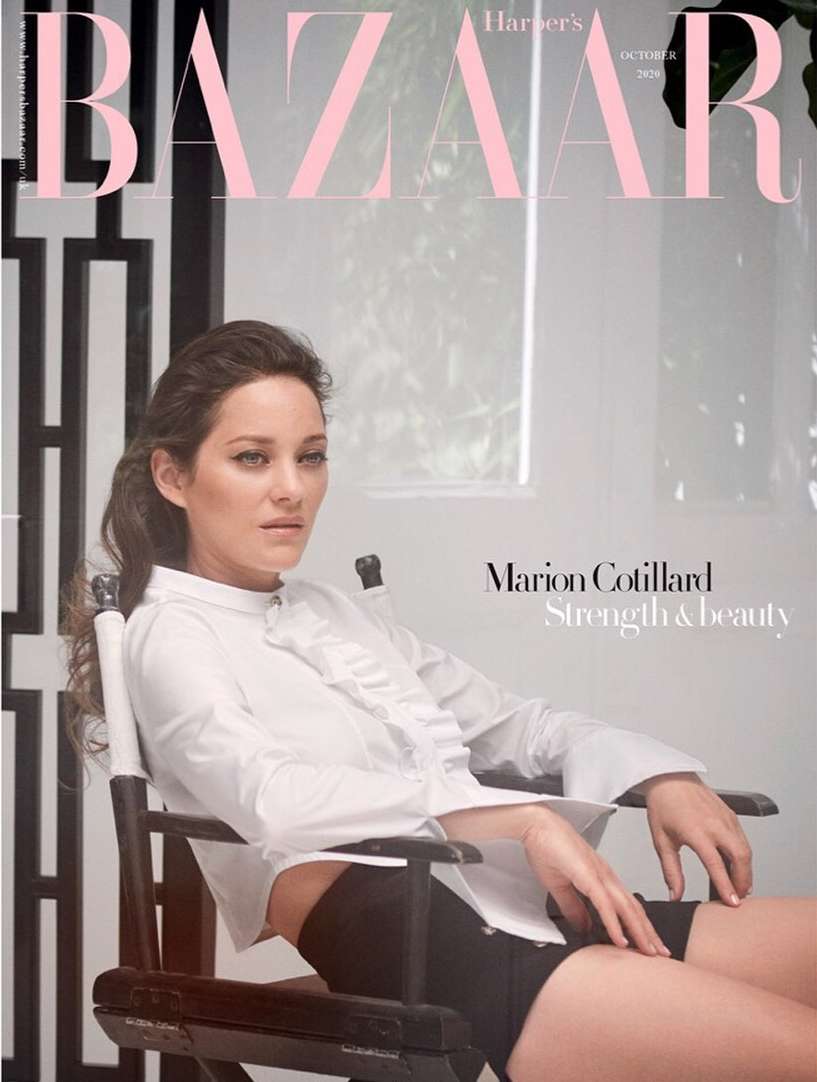 Magazine cover featuring Marion Cotillard in a white blouse and black shorts, seated in a director's chair against a bright background.