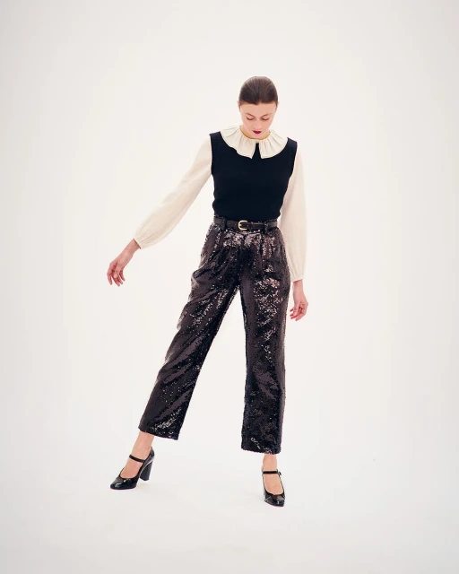 Elegant fashion shoot featuring a young woman in a white blouse, black vest, sequined pants, and Mary Jane shoes against a white backdrop.