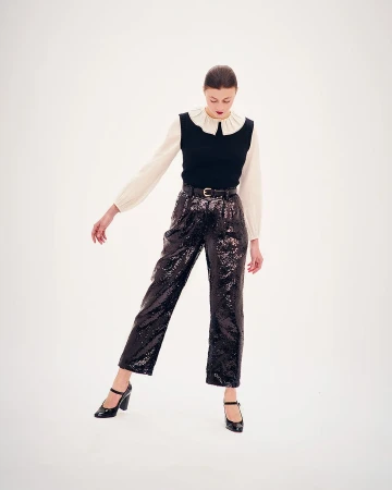 Elegant fashion shoot featuring a young woman in a white blouse, black vest, sequined pants, and Mary Jane shoes against a white backdrop.