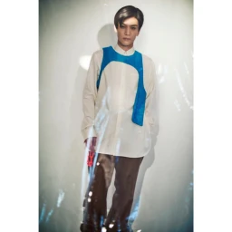 Portrait of a man in a cream shirt wearing a bright blue harness over dark trousers against a white seamless background.