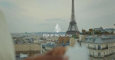 Eiffel Tower view with cityscape rooftops, sky, and Four Seasons logo. Urban Paris scene with landmark architecture.